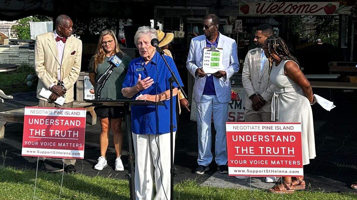 Members of a group promoting the plan to develop Pine Island into a golf course look in confusion as vocal critic of the development, Arnold Brown, joins them sporting green “support the CPO” stickers.