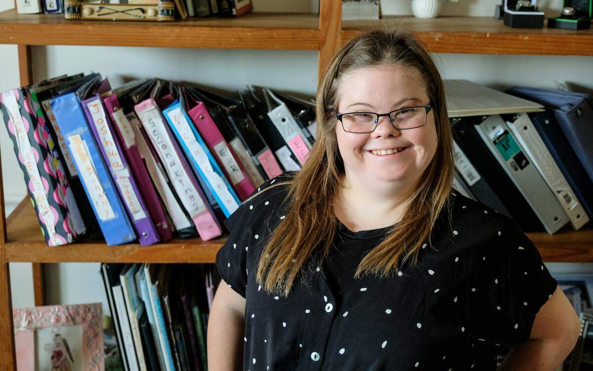 Caroline Campbell, 28, stands in front of 43 binders holding chapters of her handwritten, word-for-word transcriptions of the New American Standard version of the Bible on Thursday, May 27, 2021 in her Beaufort home. Campbell, who has Down syndrome, started with one verse in January 2012 and on Sunday June 9, she’ll finish transcribing the entire Bible with the last sentence standing in front of her congregation at Community Bible Church, almost a decade later.