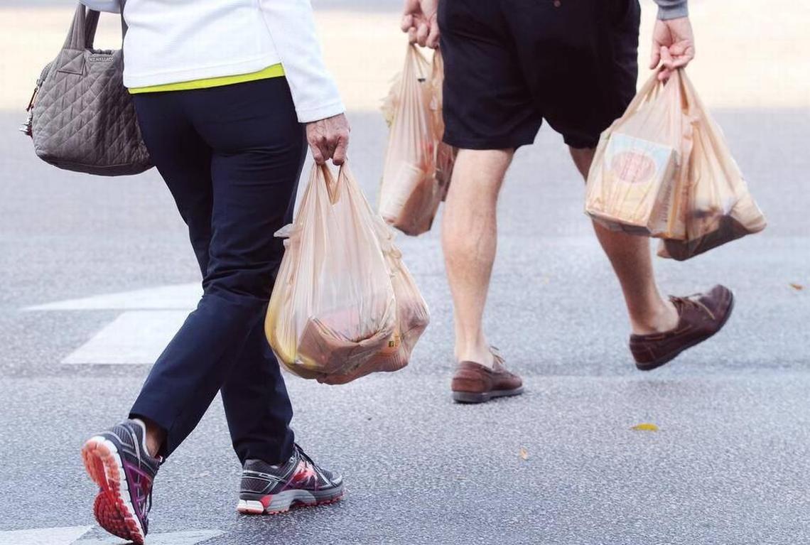 Shoppers leave a store with their groceries in plastic bags.