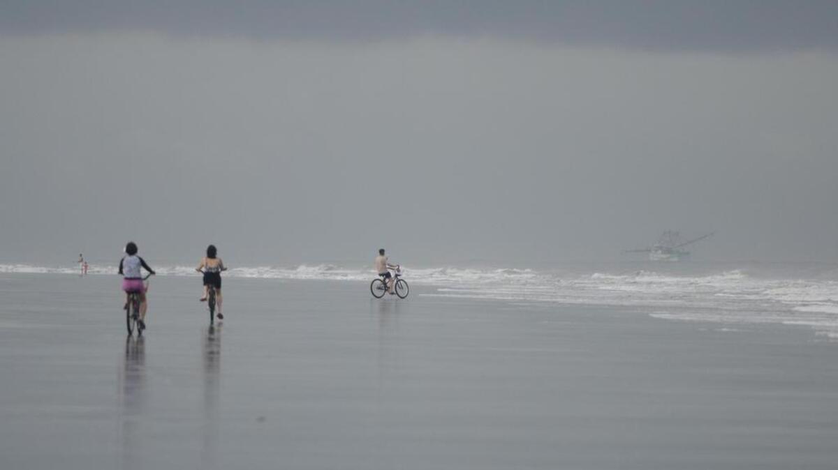 In this file photo, beachgoers bike down Hilton Head’s North Forest Beach in the sprinkling rain as a shrimp boat trawls in the distance on Tuesday.