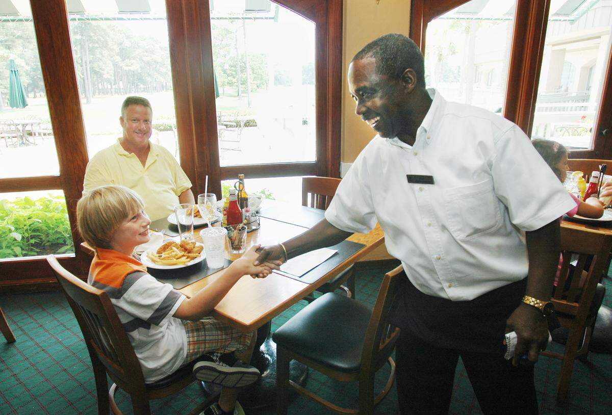 Harbour Town Grill icon Earl “Happy” Mitchell greets Jonathan Bottoms, 11, of Richmond, Va., who was eating lunch at the grill with his father Ernie in this file photo from 2009. Mitchell, a cheerful presence who lives up to his nickname, was retiring after a 45-year career with Sea Pines Resort. “There is only one Happy,” said Fred Kruge, director of food and beverage at Sea Pines.