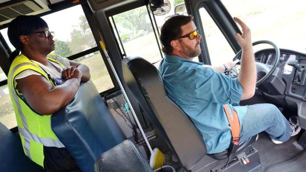 Trainer Laura Brown Spencer looks on as school bus driver trainee Rob McComas takes a practice run on a school bus on March 22, 2017 in Beaufort. A shortage of bus drivers means some after school routes sometimes have to be run twice, forcing students to wait at the bus parking lot for the bus to come back for them. Here, he motions to imaginary children to board the bus while practicing a pick-up.