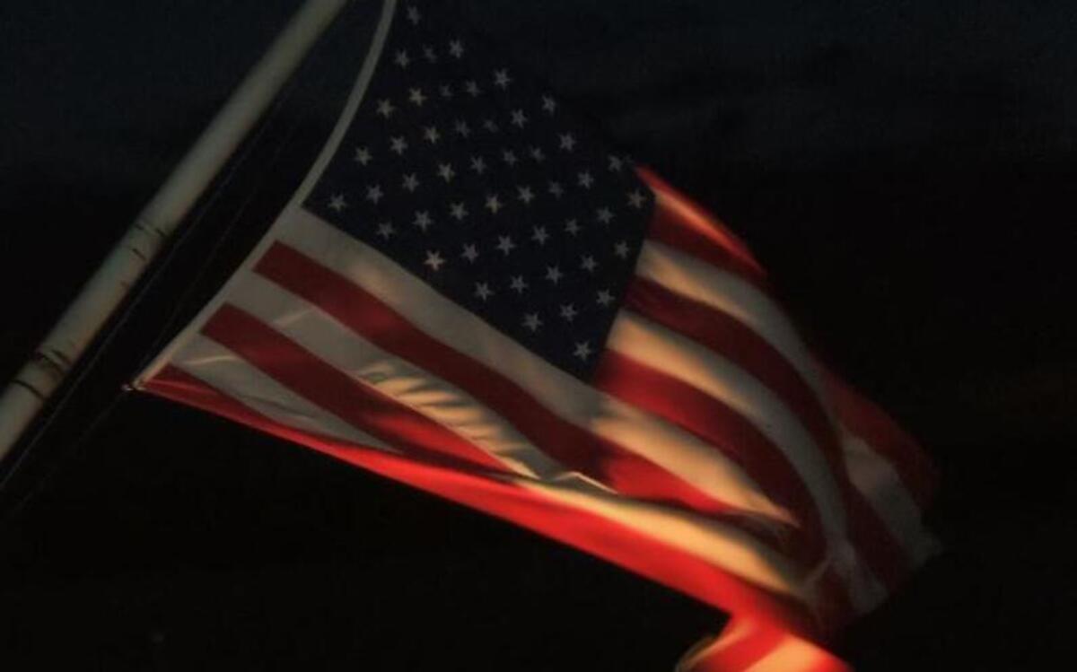 A spot-lighted Old Glory unfurls in the evening breeze.