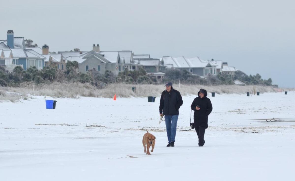 A couple and their dog walk along a stretch of North Forest Beach on Hilton Head Island that was transformed into a winter wonderland by a snowstorm on Wednesday afternoon.