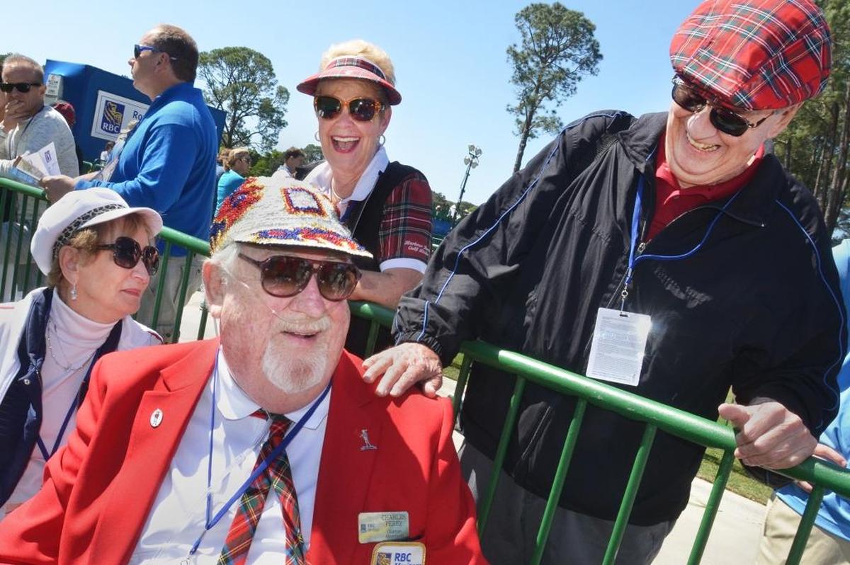 Between groups of golfers arriving on the ninth green, Heritage chairman of announcers Charles Perry, foreground, shares a laugh with friends Bill Clark and Mary Princing and Lene Toth, left, while modeling one of his many Heritage-themed caps during the third round of the RBC Heritage Presented by Boeing. Perry, who is in recovery from lung cancer and uses oxygen from a portable carrier he brings with him to the green, has been announcing arriving groups of golfers on the ninth and 18th holes for 30 years.