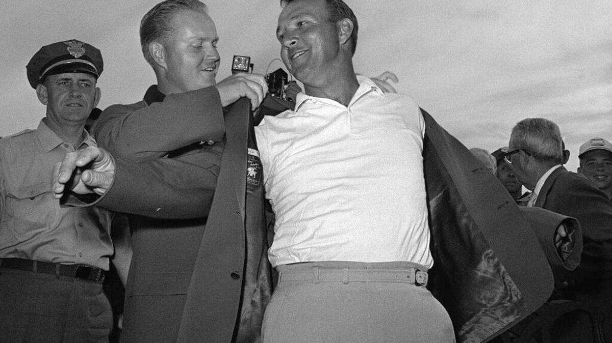 Arnold Palmer, right, slips into his green jacket with help from Jack Nicklaus after winning the Masters golf championship, in Augusta, Ga., on April 12, 1964. It was his seventh major. He was 34, the King. The golfing legend has died at the age of 87.