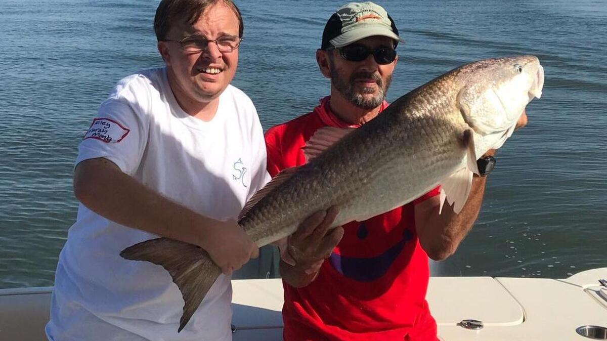 Riley Lewis, left, helps hold a bull redfish.